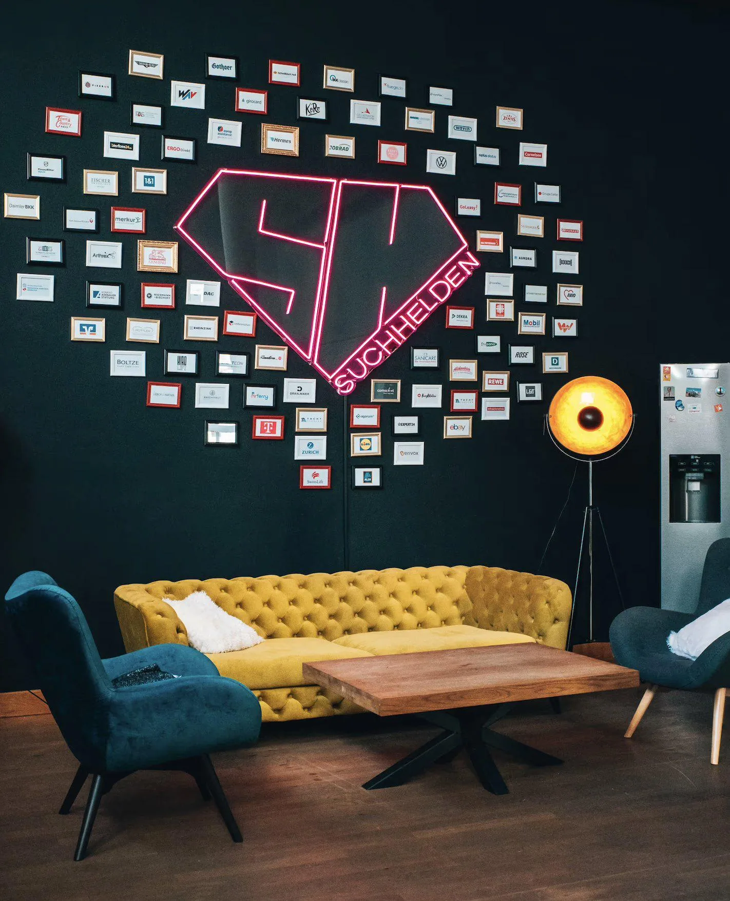 Hall of Fame: Kundenwand mit gerahmten Logos rund um das Suchhelden-Neonlogo im Büro Osnabrück